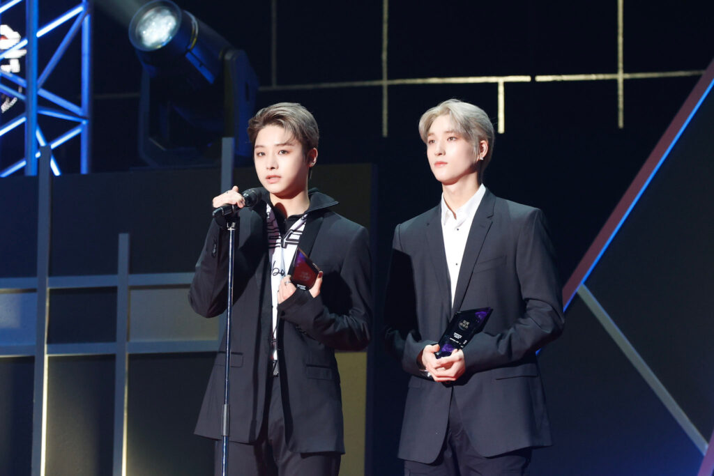 2 XODIAC members wearing black and white suits at the microphone to accept award.