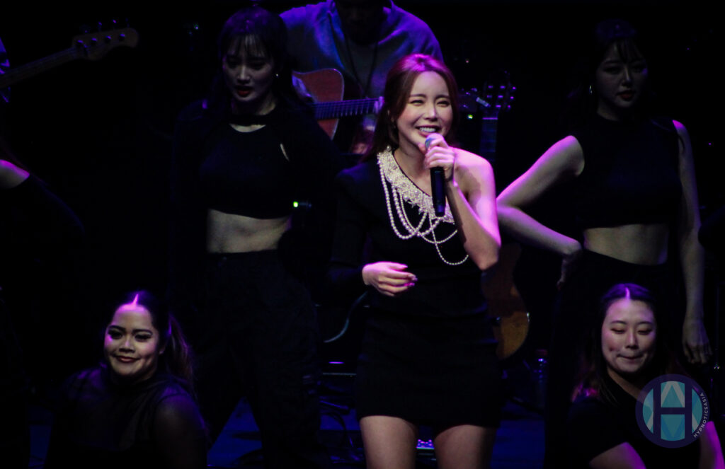 Hong Jin Young in black dress and white pearls with backup dancers
